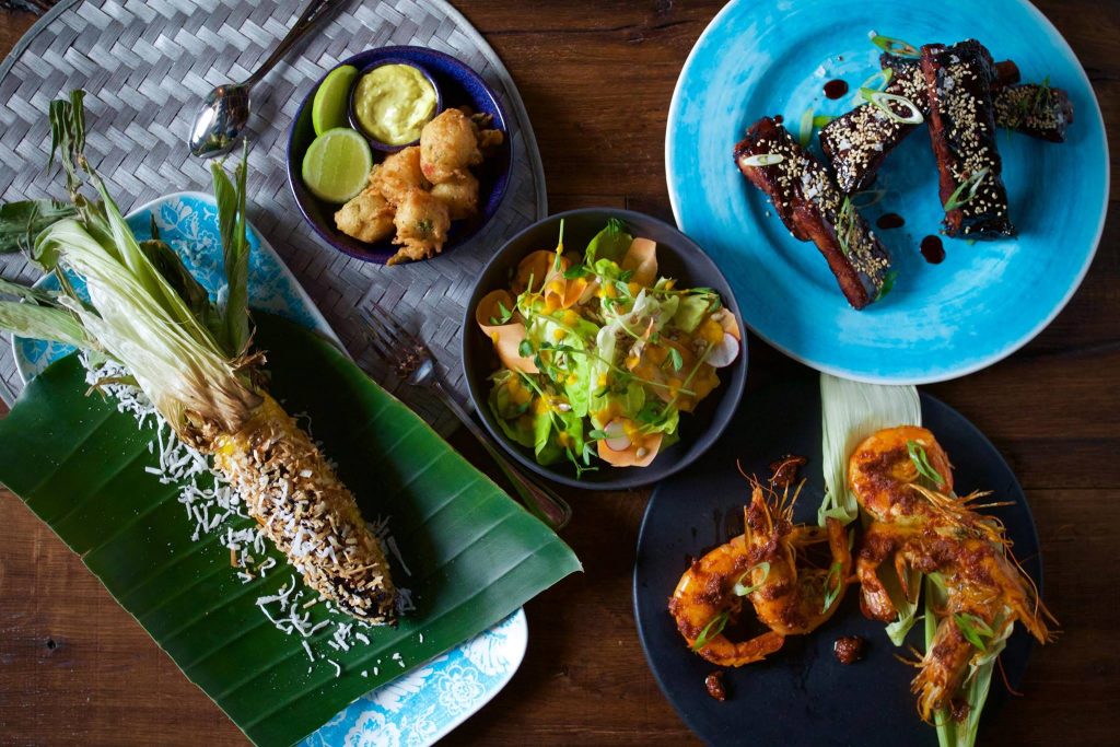 looking down onto blue, green and grey plates of colorful food on a brown wood table