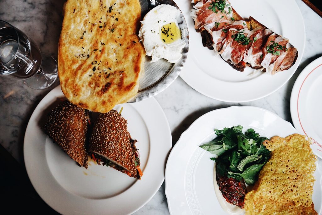 looking down onto yellow, brown and green food on white plates on a grey table, Dirty French nyc