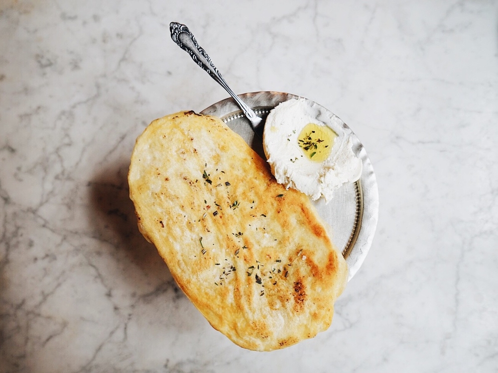 Yellow coloured Herbed flatbread with fromage blanc on a silver platter with a silver spoon 