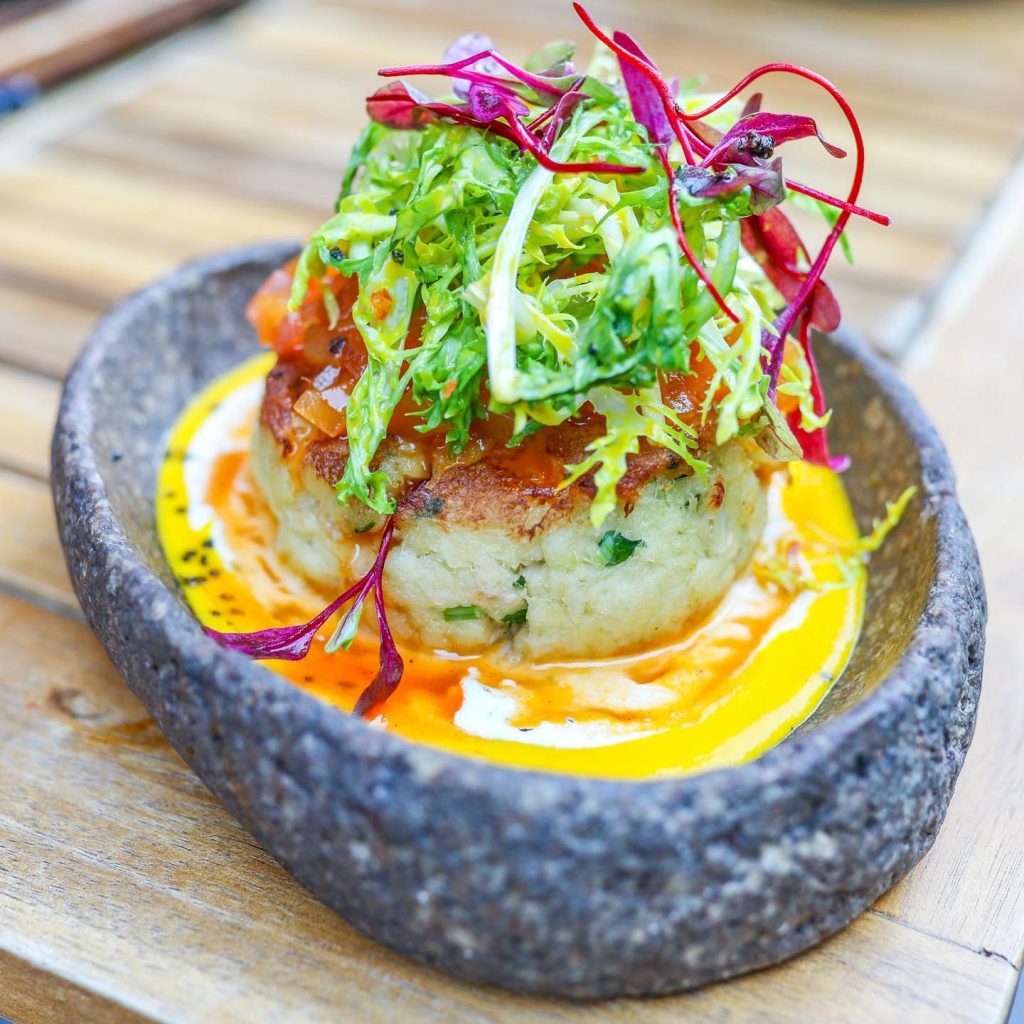 blue grey bowl of food with yellow sauce and green shoots and leaves on top