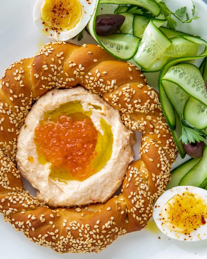 seasame seed topped round bread with a yellow and white boiled egg and chopped green cucumber